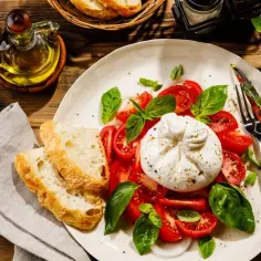 Pyszna burrata co to? Kremowy ser otoczony pomidorami i bazylią, podany z chrupiącym pieczywem i oliwą.