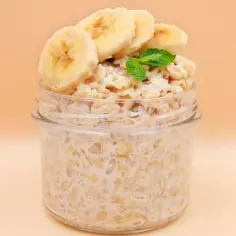 Słoik pełen kremowej owsianki z bananem, udekorowany plasterkami banana i listkiem mięty. Idealne śniadanie.