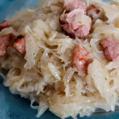 Zasmażana kapusta z kawałkami boczku na niebieskim talerzu.
