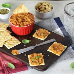 Kremowa pasta z suszonych pomidorów na krakersach, podana z ziołami i orzechami.