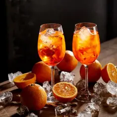 Dwa kieliszki Aperol Spritz z lodem i pomarańczami na drewnianym stole.