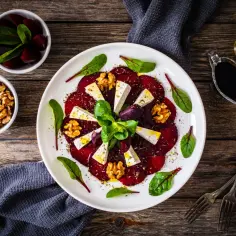 Carpaccio z buraka z serem feta, orzechami i ziołami na białym talerzu.
