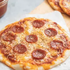 Pyszna pizza z tortilli na patelni, z serem i pepperoni, gotowa do podania. Obok sos i łyżeczka.