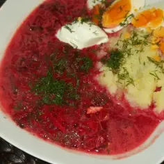 Zupa botwinkowa z ziemniakami, jajkiem i śmietaną, ozdobiona koperkiem.