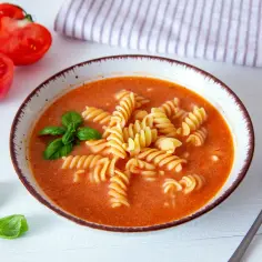 Miseczka zupy pomidorowej z makaronem fusilli, pomidorami i bazylią.