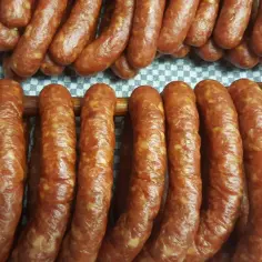 Prawdziwa wiejska kiełbasa przepis: świeżo uwędzone, rumiane kiełbaski wiszą na drewnianych drążkach, gotowe do spożycia.