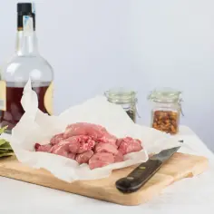 Surowa grasica na papierze, obok butelka alkoholu, liście laurowe i przyprawy.