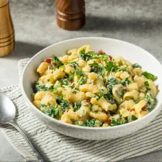 Miska makaronu z szpinakiem, suszonymi pomidorami i parmezanem, udekorowana natką pietruszki.
