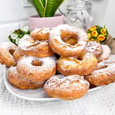 Stos puszystych, domowych oponków posypanych cukrem pudrem, gotowych do schrupania.