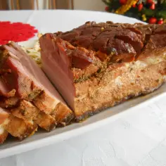 Pyszny boczek pieczony w rękawie, pokrojony w plastry, prezentuje się apetycznie na białej zastawie. W tle choinka.