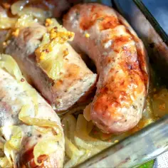 Pieczona biała kiełbasa surowa z cebulą i musztardą w naczyniu żaroodpornym.