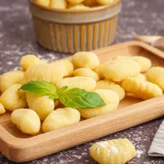 Pyszne, domowe gnocchi na drewnianej desce, gotowe na pyszny sos. Obok czosnek i świeża bazylia. Idealny przepis na gnocchi z sosem.