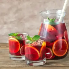 Dzbanek i dwa kieliszki z sangrią, owocami i miętą na drewnianym stole.