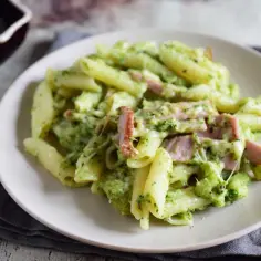 Penne z brokułami i kawałkami szynki w kremowym sosie śmietanowym, posypane serem. Pyszne danie obiadowe.