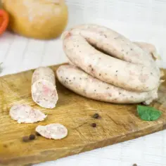 Biała kiełbasa na desce, gotowa do przygotowania według przepisu. W tle pomidor i chleb.