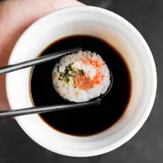 Pałeczki trzymają sushi z łososiem, zanurzając je w ciemnym sosie do sushi.