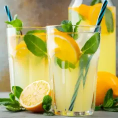 Dwa szklanki orzeźwiającej lemoniady z cytryną i miętą, obok cytryny i dzbanka.