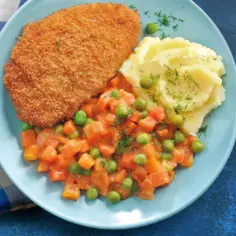 Kotlet panierowany z puree ziemniaczanym i warzywami na talerzu.