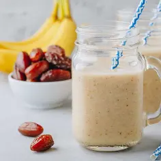 Pyszny szejk bananowo-daktylowy w słoiczkach, obok miseczka daktyli i banany. Idealny na szybkie śniadanie.