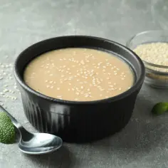 Miseczka z tahini posypana sezamem, obok łyżka i listki mięty.