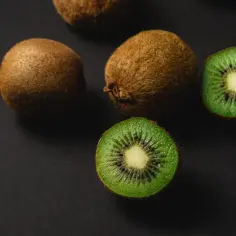 Kilka owoców kiwi, w tym dwa przekrojone na pół, na ciemnym tle.