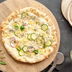 Pyszna pizza bianca z cukinią, cebulą i cytryną, posypana parmezanem i ziołami.