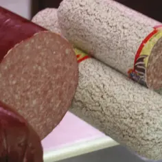 Kawałki ciemnej i jasnej kiełbasy salami, jedna przekrojona.