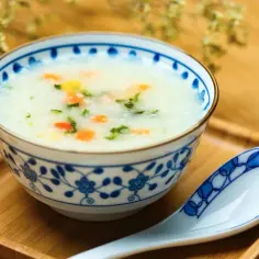Miseczka z congee, ryżową potrawą z warzywami, obok łyżki na drewnianej tacce.