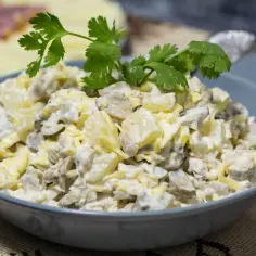 Sałatka z pieczarkami, jajkiem i serem w szarej misce, ozdobiona natką pietruszki.