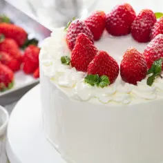 Puszysty tynk do tortu z mascarpone, ozdobiony świeżymi truskawkami i listkami mięty. Idealny na letnie przyjęcie.