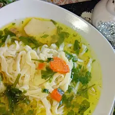 Klarowny rosół z perliczki z makaronem, marchewką i natką pietruszki w białej misce.