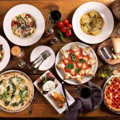 Obficie zastawiony stół z pysznymi włoskimi daniami: pizze, makarony, ravioli, sałatka i przystawki.