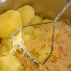 Gotowane ziemniaki i kapusta kiszona w garnku, z widocznym tłuczkiem do ziemniaków.