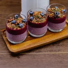 Szybki deser z niczego: pudding chia z jagodami i granolą w szklankach na drewnianej tacy.
