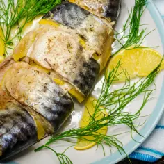 Pieczona makrela z cytryną i koperkiem na talerzu, obok sztućce.