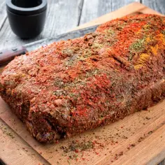 Surowy schab pokryty przyprawami na desce do krojenia.