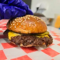 Rękawiczka zakłada górną bułkę na soczystego smash burgera z serem i ogórkiem. Tak wygląda idealny smash burger co to.