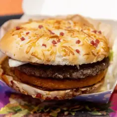 Apetyczny burger drwala z podwójnym mięsem, chrupiącym plackiem ziemniaczanym i bułką posypaną serem i kawałkami boczku.