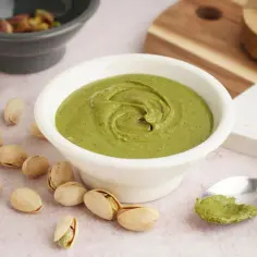 Pyszny krem pistacjowy w miseczce, otoczony łuskanymi pistacjami. Idealny przykład, jak zrobić krem pistacjowy.