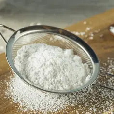 Cukier puder przesiewany przez sitko na drewnianej desce.