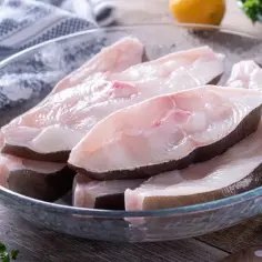 Surowe kawałki halibuta w szklanej misce, gotowe do przygotowania.