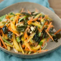 Kolorowa sałatka wakame z mango, marchewką i orzeszkami ziemnymi, posypana sezamem.