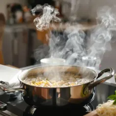 Para dowodzi, jak ugotować makaron. Garnek z wrzącą wodą i makaronem na płycie indukcyjnej, obok miseczka z tartym serem.