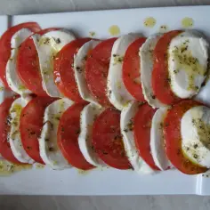 Wyśmienita mozzarella z pomidorami, skropiona oliwą i ziołami, ułożona na białym talerzu.