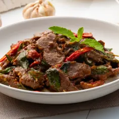 Aksamitne kawałki wołowiny po tajsku z bazylią i papryczką chili, podane w białej misce.