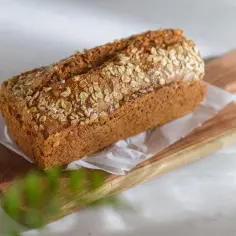 A freshly baked chleb owsiany z płatkami owsianymi na wierzchu, ułożony na drewnianej desce.