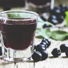 Szklanka z ciemnym nalewem aroniowym, obok owoce aronii i liście.