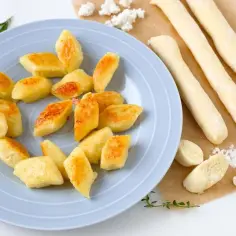 Usmażone kopytka na talerzu i surowe wałeczki ciasta obok. Dowiedz się, ile gotować kopytka, by były idealne.