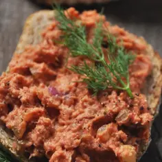 Kanapka z pastą z makreli w pomidorach, ozdobiona koperkiem.