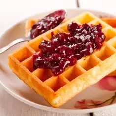 Gofry z frużeliną wiśniową na talerzu z kwiatowym wzorem.